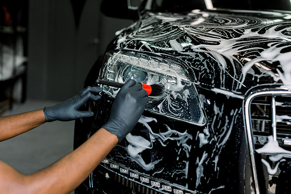 A Lumera Detail detailer carefully washing a car's headlight and bonnet